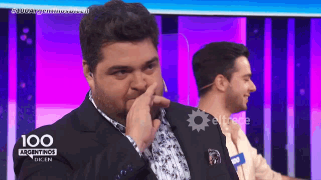 a man in a suit is covering his nose in front of a screen that says 100 argentinos dicen