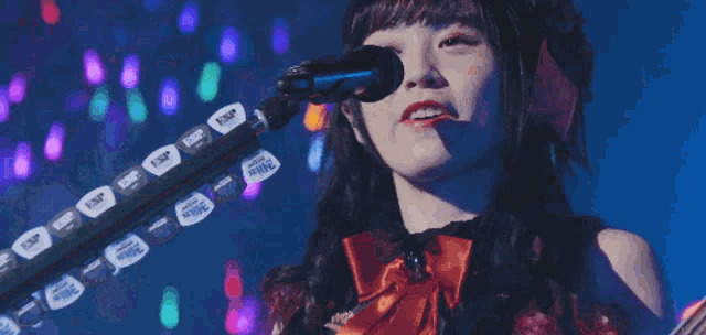 a woman singing into a microphone with a guitar in the background