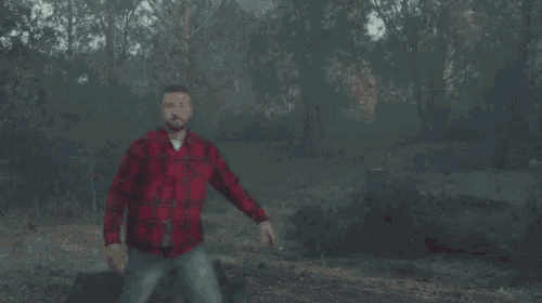 a man in a plaid shirt is dancing in the woods while pointing at something .