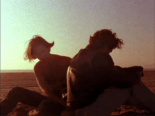a man and a woman sit on a rock on the beach