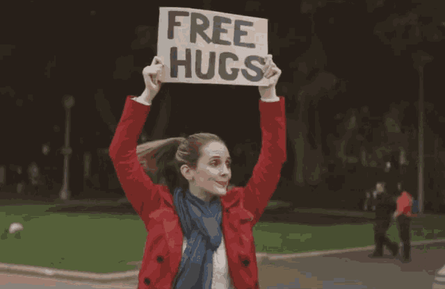 a woman in a red coat holds up a sign that reads free hugs