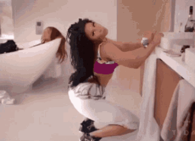 a woman is kneeling down in front of a sink in a bathroom while another woman sits in a bathtub