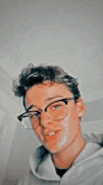 a young man wearing glasses and a hoodie is smiling .