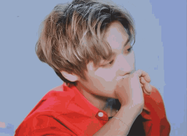 a young man wearing a red shirt is covering his mouth with his hands