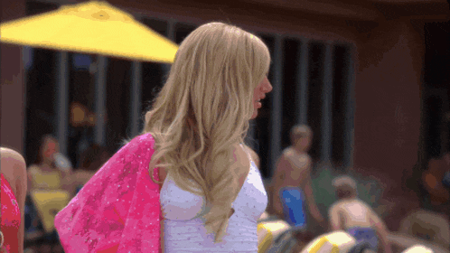 a woman wearing a white top and a pink bag is standing in front of a yellow umbrella
