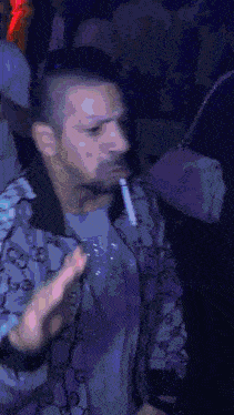 a man in a gucci jacket is smoking a cigarette in a nightclub .