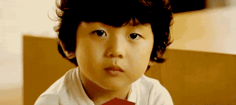 a young boy with curly hair looks at the camera with a serious look on his face
