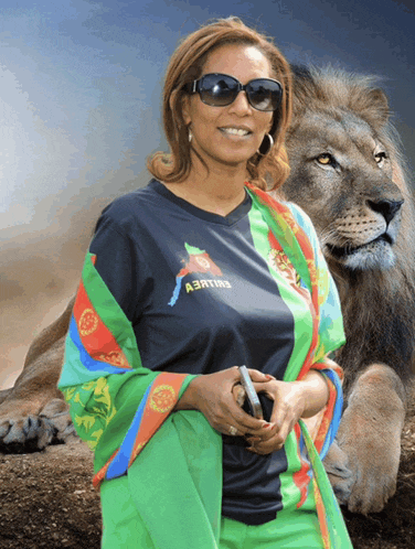 a woman wearing a shirt that says a3rting stands next to a lion