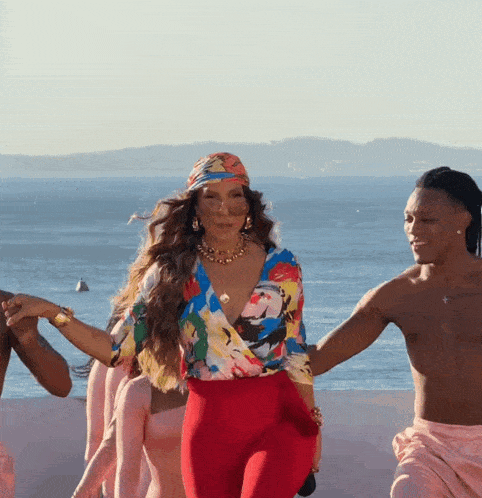a woman in a colorful top and red pants is dancing with a group of men