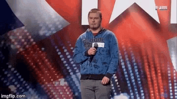 a man in a blue hoodie is standing on a stage holding a microphone and singing into it .