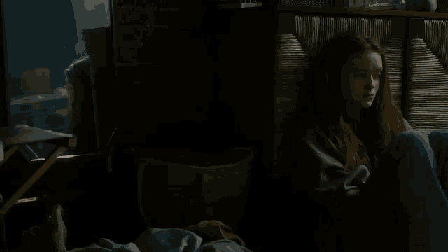 a woman with red hair sits in a dark room