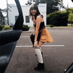 a woman in a yellow skirt and white socks is standing in front of a car door