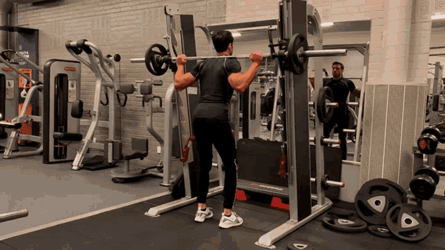 a man squatting with a barbell in a gym with a mirror