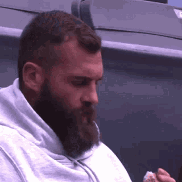 a man with a beard wearing a grey hoodie is eating something