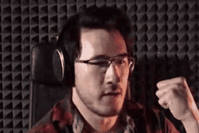 a man wearing headphones and glasses is flexing his muscles in front of a microphone in a recording studio .