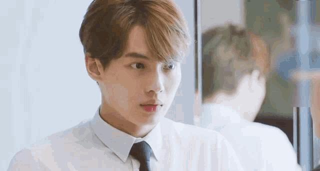 a young man wearing a white shirt and tie is standing in front of a mirror .