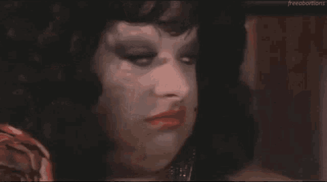 a close up of a drag queen 's face with red lipstick and black eyeshadow .