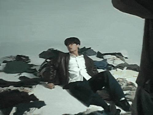 a man in a leather jacket is sitting on a pile of clothing