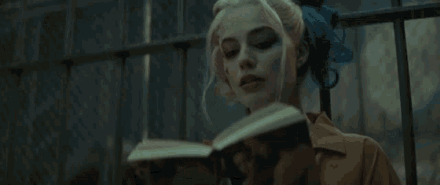harley quinn is reading a book while holding a mug of coffee .