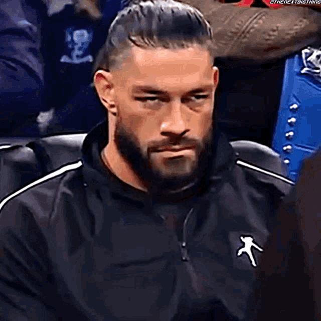 roman reigns is sitting in a chair with his eyes closed and a beard .