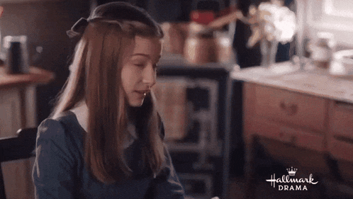 a girl in a blue dress is sitting at a table in a hallmark drama scene .
