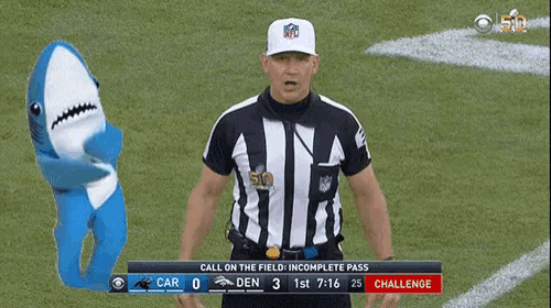 a referee stands on a field with a shark mascot behind him