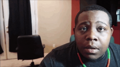 a man wearing a black shirt and a green and red necklace is looking at the camera