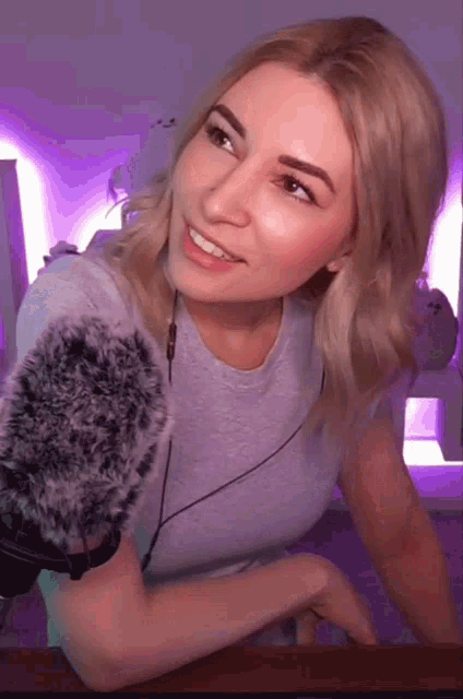 a woman in a grey shirt is smiling in front of a purple background