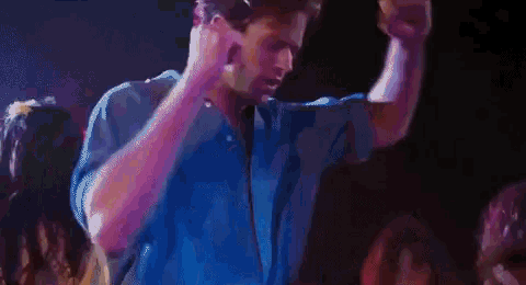 a man in a blue shirt is singing into a microphone while dancing in front of a crowd .