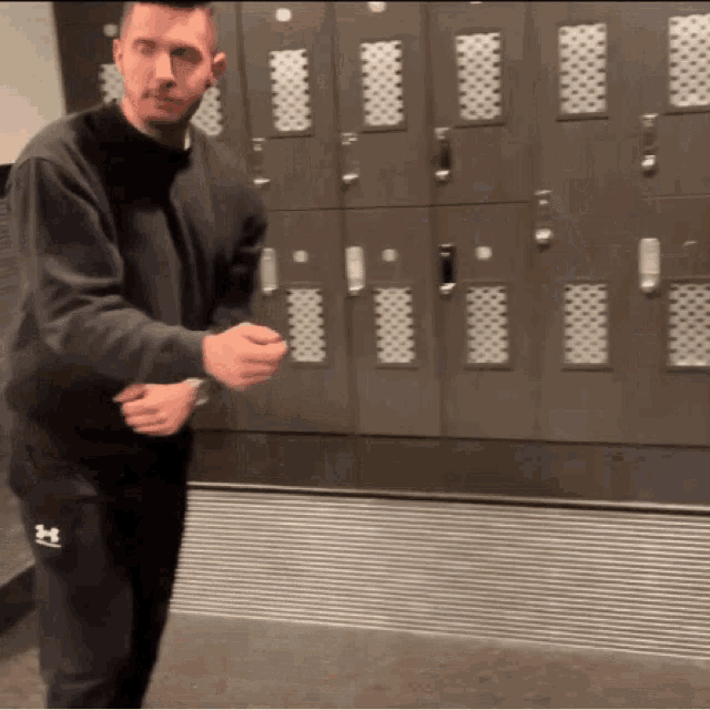 a man wearing under armour sweatpants is standing in front of a row of lockers