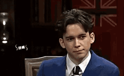a man in a suit and tie is sitting in a chair and looking at the camera .