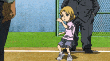 a little girl in a pink shirt and blue shorts stands on a baseball field