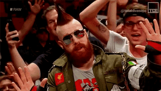a man wearing sunglasses and a green jacket is surrounded by a crowd .