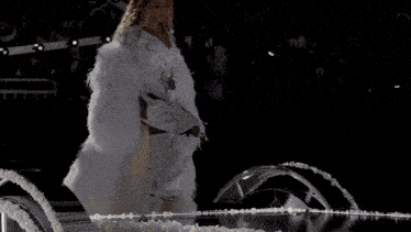 a woman in a white fur coat is walking across a stage .