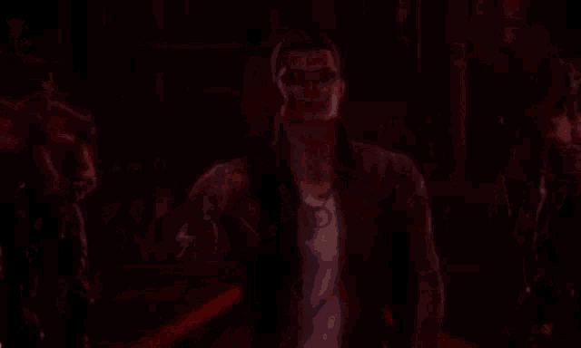 a man with glasses and a tattoo on his arm stands in front of a group of red men