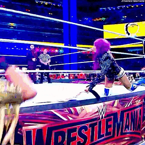 a woman with purple hair is kneeling down in a wrestling ring while a referee watches .