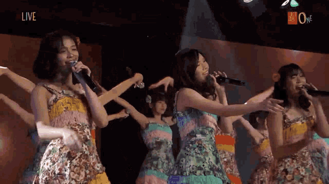 a group of women singing into microphones with the word live on the bottom right