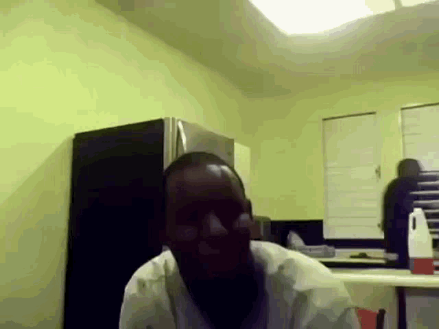a man in a white shirt is sitting in a kitchen with a black refrigerator behind him