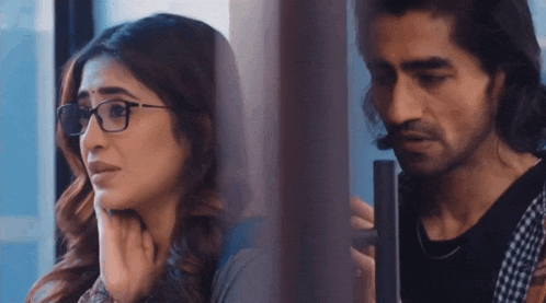 a man and a woman are looking out of a window . the woman is wearing glasses .