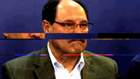 a man with glasses and a mustache looks at the camera with a blue background