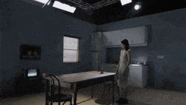 a woman in a white dress stands in a dark kitchen