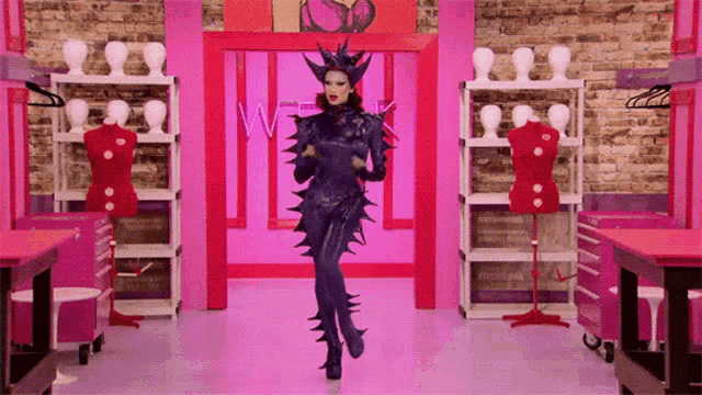 a woman in a drag queen costume stands in a room with mannequins and a sign that says wigs