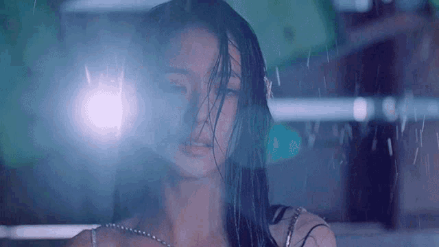 a woman with wet hair is standing in the rain with a light behind her .