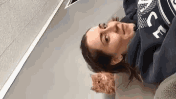 a woman in a blue sweatshirt is laying on a bed next to a cat .