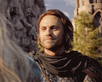 a man with long hair and a scarf around his neck stands in front of a mountain