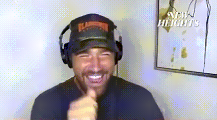 a man wearing headphones and a flamingo hat is smiling and pointing at the camera .
