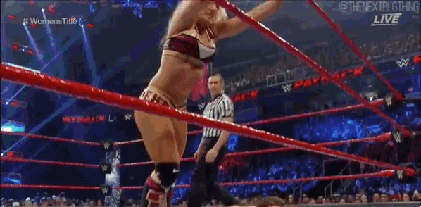 a woman is laying on the ground in a wrestling ring with a referee in the background .