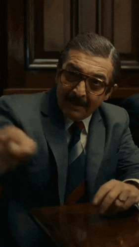 a man in a suit and tie is sitting at a table with his hands outstretched