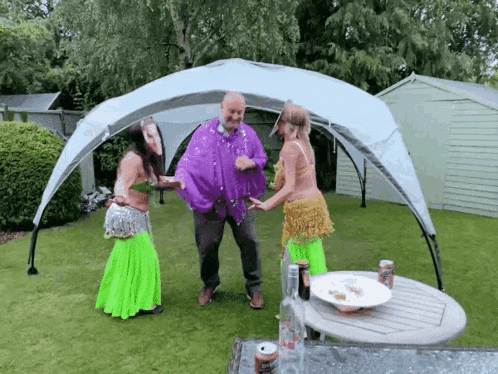 a man and two women are dancing under a canopy in a garden