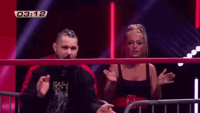 a man and a woman are standing in a wrestling ring with the time 03:11 on the screen behind them .